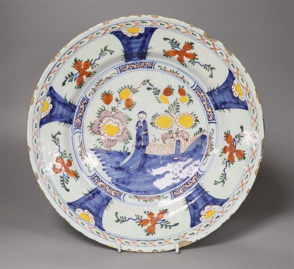 A large polychrome Delft charger, painted with a central figure beside a walled garden, set within floral borders, in the Chinese taste